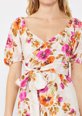 [Color: Natural/Orchid] A blonde model wearing a pretty floral mini dress in pink and orange. With a surplice v neckline, puff sleeves, attached waist belt with multiple styling opportunities, and smocked back. A floral fall dress for special occasions and dinner parties.