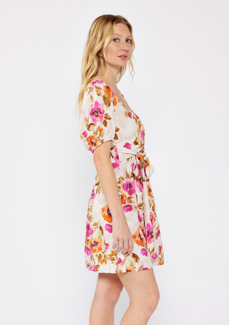 [Color: Natural/Orchid] A blonde model wearing a pretty floral mini dress in pink and orange. With a surplice v neckline, puff sleeves, attached waist belt with multiple styling opportunities, and smocked back. A floral fall dress for special occasions and dinner parties.