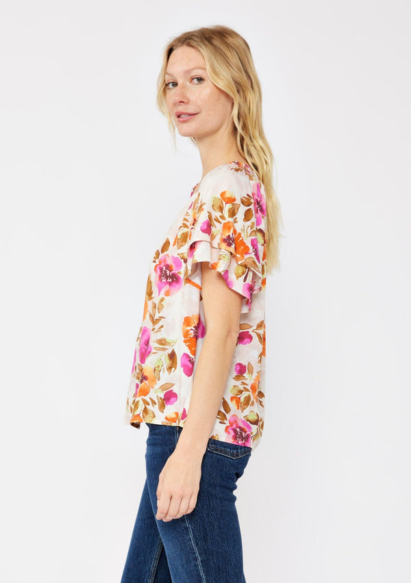 [Color: Natural/Orchid] A blonde model wearing a relaxed fit top in a floral print. With short double flutter sleeves, split v neckline, and a smocked detail at the neck. A dressy but casual floral top styled with dark denim.