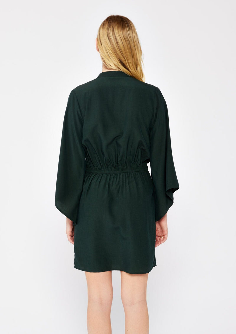 [Color: Olive] A blonde model wearing a green dark olive mini dress. With a deep v-neckline, front hook and eye closure, front tie waist detail, flared long sleeves , and a relaxed fit. A dressy but casual fall dress.