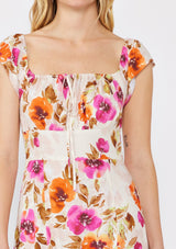 [Color: Natural/Orchid] A blonde model wearing a large floral print maxi dress in orange and pink florals. With a square neckline, tie front neckline detail, smocked back, flutter cap sleeves, and a side slit. 