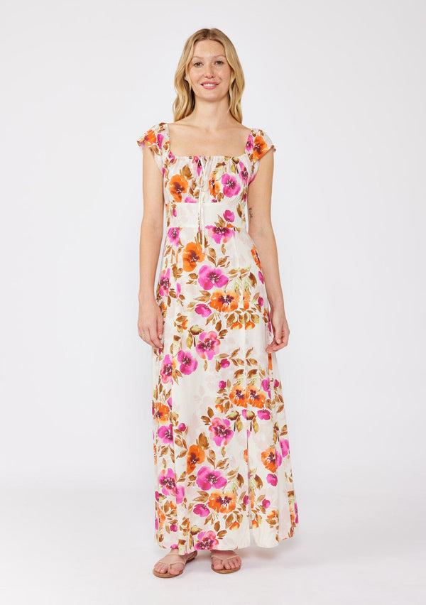 [Color: Natural/Orchid] A blonde model wearing a large floral print maxi dress  in orange and pink florals. With a square neckline, tie front neckline detail, smocked back, flutter cap sleeves, and a side slit. A fall maxi dress paired with strappy sandals. 