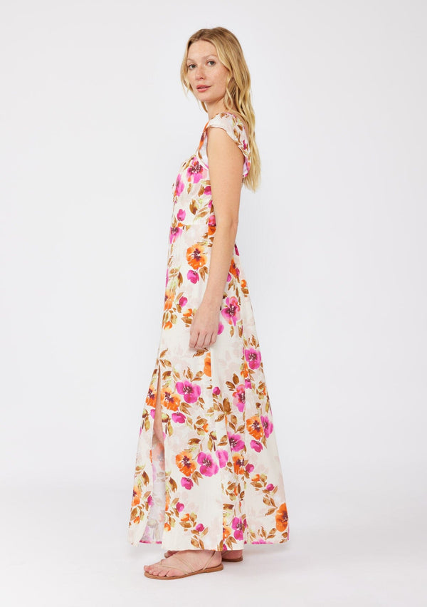 [Color: Natural/Orchid] A blonde model wearing a large floral print maxi dress in orange and pink florals. With a square neckline, tie front neckline detail, smocked back, flutter cap sleeves, and a side slit. A fall maxi dress paired with strappy sandals.