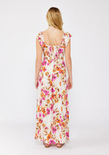 [Color: Natural/Orchid] A blonde model wearing a large floral print maxi dress in orange and pink florals. With a square neckline, tie front neckline detail, smocked back, flutter cap sleeves, and a side slit. A fall maxi dress paired with strappy sandals.