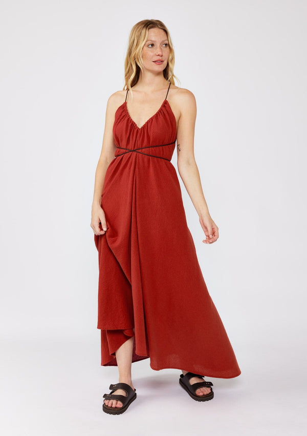 [Color: Sienna]  A blonde model wearing an ultra bohemian Fall maxi dress with slip on chunky sandals. A cotton maxi dress in a red wine solid print, ruched v neckline, adjustable braided straps, open cross back, and relaxed fit. A casual cotton maxi for a dreamy summer to fall transition.  
