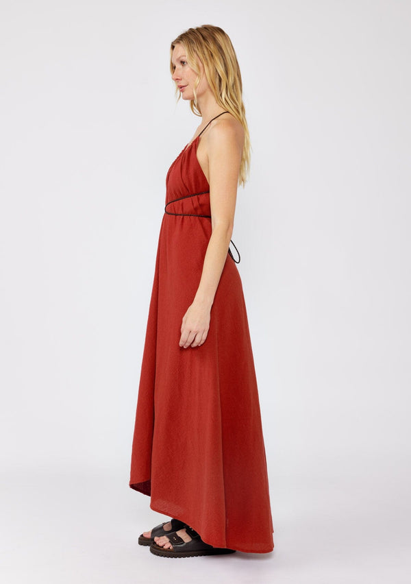 [Color: Sienna] A blonde model wearing an ultra bohemian Fall maxi dress with slip on chunky sandals. A cotton maxi dress in a red wine solid print, ruched v neckline, adjustable braided straps, open cross back, and relaxed fit. A casual cotton maxi for a dreamy summer to fall transition.