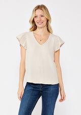 [Color: Natural] A blonde model wearing a simple neutral beige top with a v neckline and flutter short sleeves. A soft cotton gauze top paired with dark denim for a casual day out. 