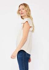[Color: Natural] A blonde model wearing a simple neutral beige top with a v neckline and flutter short sleeves. A soft cotton gauze top paired with dark denim for a casual day out.