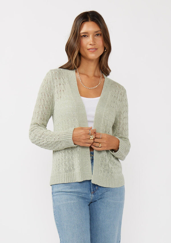 [Color: Light Sage] A front facing image of a brunette model wearing green tape yarn cardigan with open knit details. This lightweight cardigan features long sleeves, an open front, and ribbed trim, making it ideal for light layering in the spring.