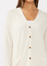 [Color: Vanilla] A detail image of a brunette model wearing an off white thin linen and viscose blend cardigan with long sleeves, a button front, and a v-neckline. An effortless basic throw on cardigan for the spring season. 