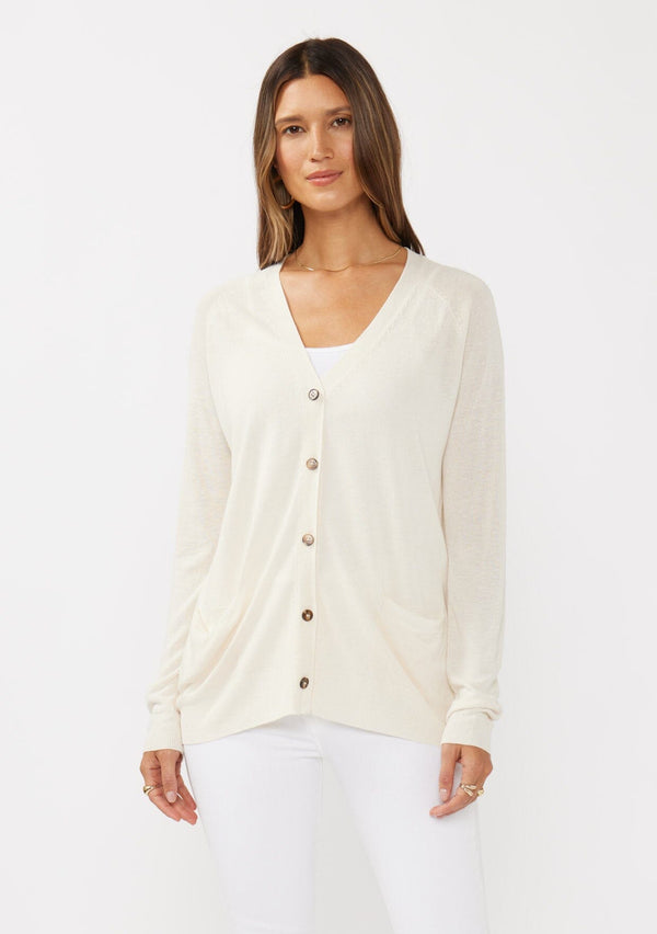 [Color: Vanilla] A front facing image of a brunette model wearing an off white thin linen and viscose blend cardigan with long sleeves, a button front, and a v-neckline. An effortless basic throw on cardigan for the spring season. 