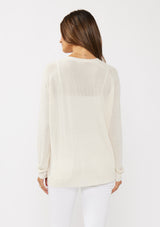 [Color: Vanilla] A back facing image of a brunette model wearing an off white thin linen and viscose blend cardigan with long sleeves, a button front, and a v-neckline. An effortless basic throw on cardigan for the spring season. 