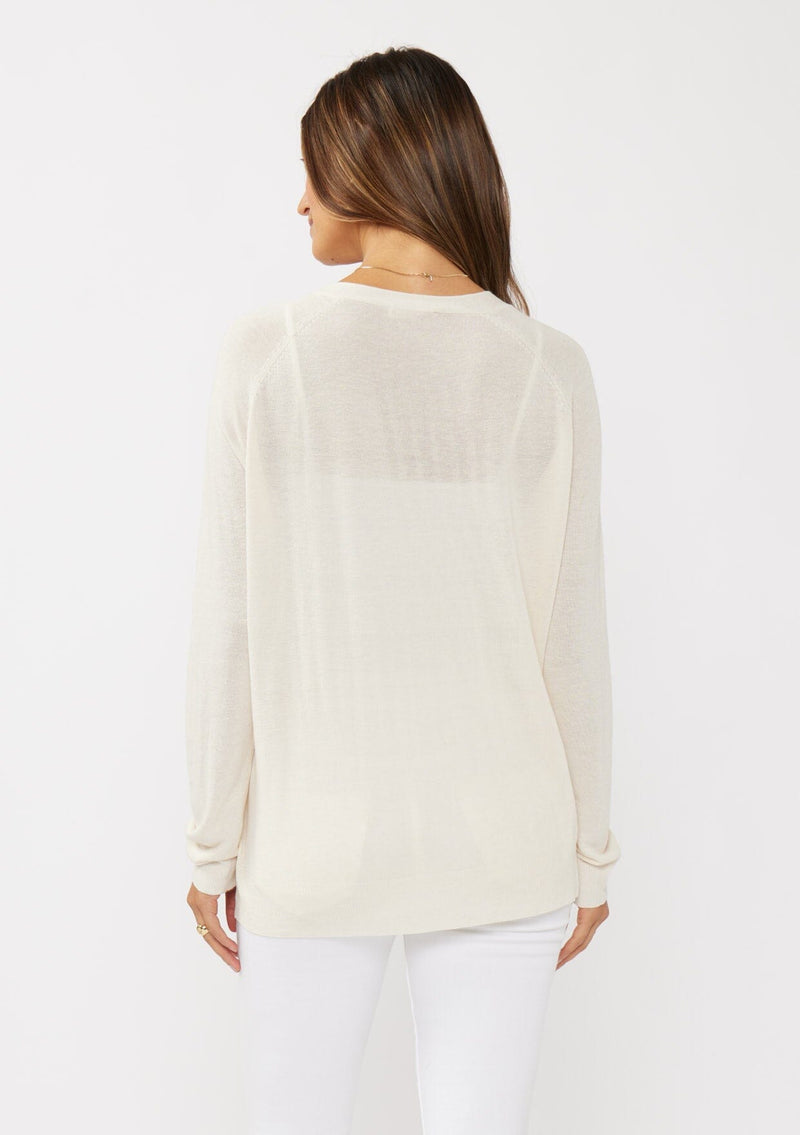 [Color: Vanilla] A back facing image of a brunette model wearing an off white thin linen and viscose blend cardigan with long sleeves, a button front, and a v-neckline. An effortless basic throw on cardigan for the spring season. 