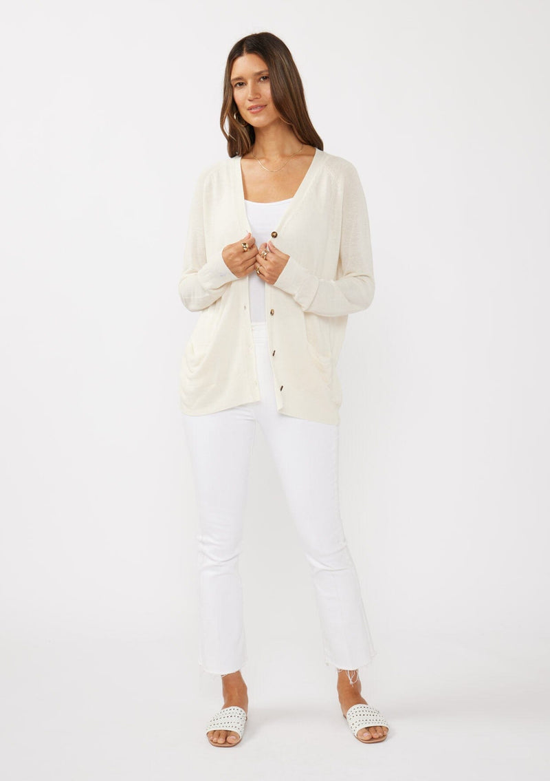 [Color: Vanilla] A front facing image of a brunette model wearing an off white thin linen and viscose blend cardigan with long sleeves, a button front, and a v-neckline. An effortless basic throw on cardigan for the spring season. 