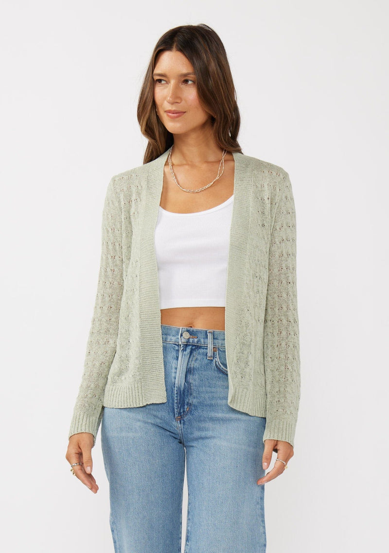 [Color: Light Sage] A front facing image of a brunette model wearing green tape yarn cardigan with open knit details. This lightweight cardigan features long sleeves, an open front, and ribbed trim, making it ideal for light layering in the spring.