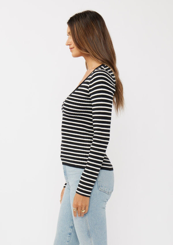 [Color: Black/White] A side facing image of a black and white striped pullover sweater with a ribbed texture, long sleeves, and a wide v-neckline. A timeless piece ideal for layering.