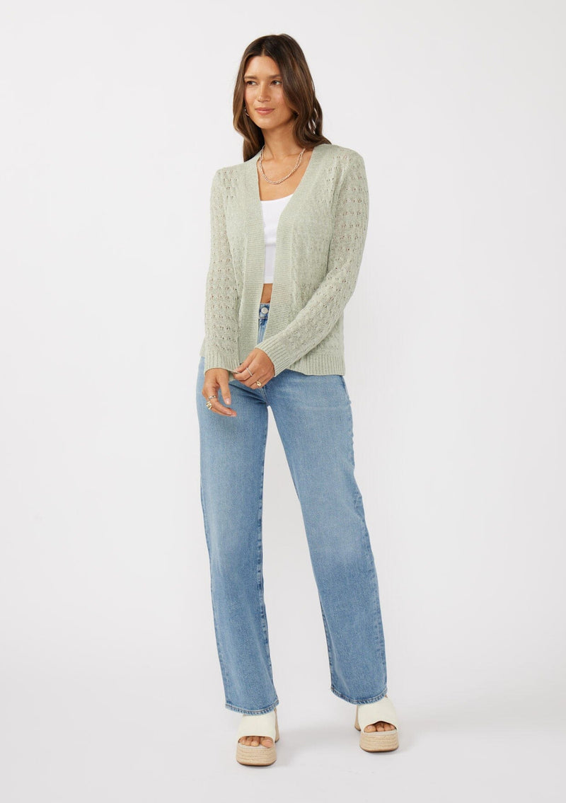 [Color: Light Sage] A front facing image of a brunette model wearing green tape yarn cardigan with open knit details. This lightweight cardigan features long sleeves, an open front, and ribbed trim, making it ideal for light layering in the spring.