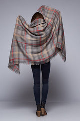 [Color: Grey/Red] A brunette model wearing an oversized grey and red plaid scarf with fringed trim, adding a versatile and eye-catching accent to her outfit.