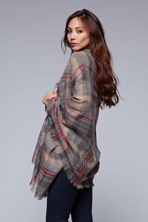 [Color: Grey/Red] A brunette model wearing an oversized grey and red plaid scarf with fringed trim, adding a versatile and eye-catching accent to her outfit.