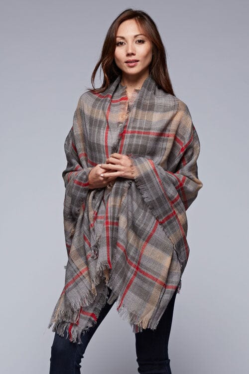 [Color: Grey/Red] A brunette model wearing an oversized grey and red plaid scarf with fringed trim, adding a versatile and eye-catching accent to her outfit.