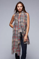 [Color: Grey/Red] A brunette model wearing an oversized grey and red plaid scarf with fringed trim, adding a versatile and eye-catching accent to her outfit.