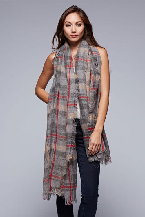 [Color: Grey/Red] A brunette model wearing an oversized grey and red plaid scarf with fringed trim, adding a versatile and eye-catching accent to her outfit.