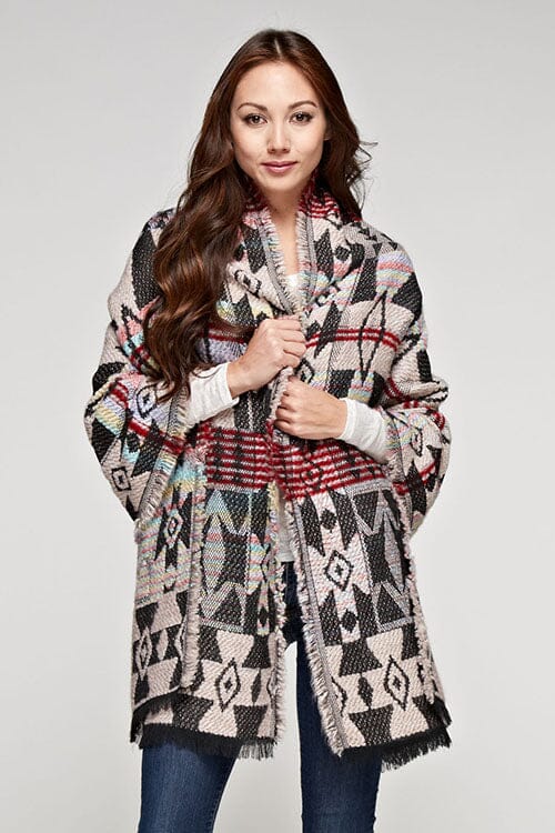 [Color: Multi/Black] A brunette woman wearing a cozy multi-color tribal print wrap poncho with fringed trim, styled as a chic layering piece for fall. Can also be worn as a thick scarf. 