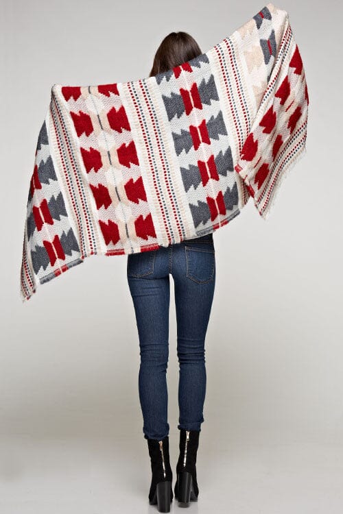 [Color: Red/Navy] A brunette model wearing a red and navy tribal print wrap poncho with fringed trim and blanket stitch details, styled as a cozy and warm layering piece.