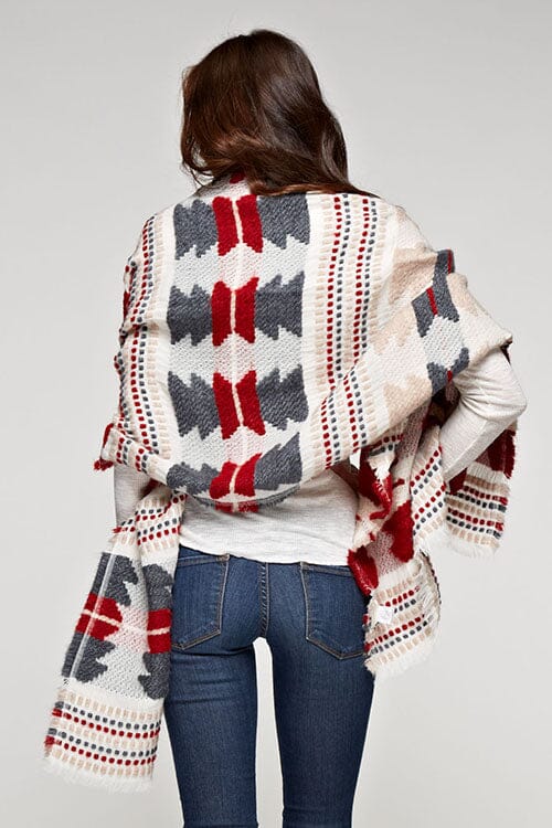 [Color: Red/Navy] A brunette model wearing a red and navy tribal print wrap poncho with fringed trim and blanket stitch details, styled as a cozy and warm layering piece.