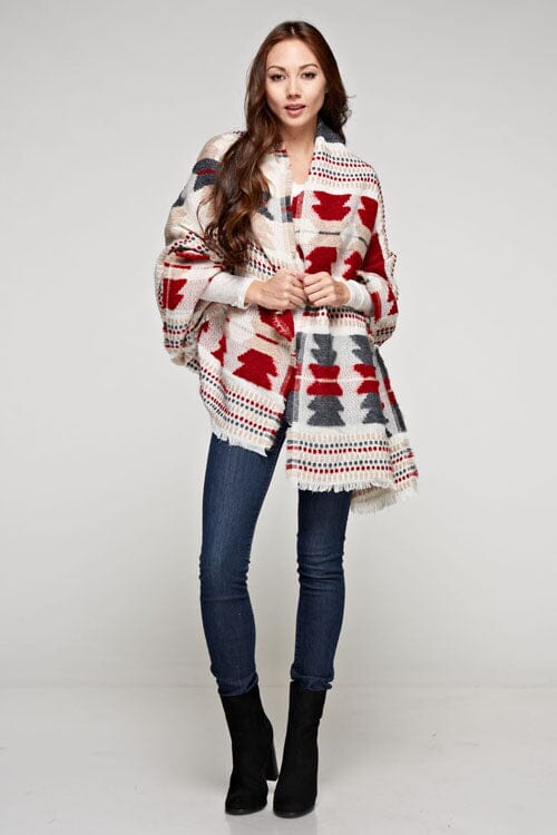 [Color: Red/Navy] A brunette model wearing a red and navy tribal print wrap poncho with fringed trim and blanket stitch details, styled as a cozy and warm layering piece.