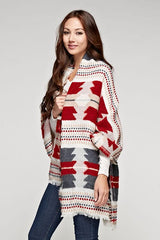 [Color: Red/Navy] A brunette model wearing a red and navy tribal print wrap poncho with fringed trim and blanket stitch details, styled as a cozy and warm layering piece.