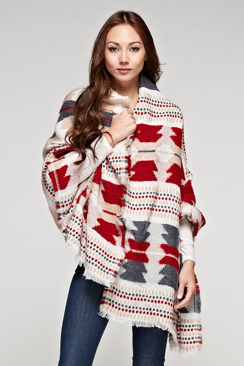 [Color: Red/Navy] A brunette model wearing a red and navy tribal print wrap poncho with fringed trim and blanket stitch details, styled as a cozy and warm layering piece.