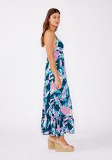 [Color: Teal/Dusty Orchid] A brunette model wearing a beautiful tropical print maxi dress with wedges. A tiered maxi dress with ruffle trim details, spaghetti straps, cross back, and v neckline. A vacation style dress with an empire waistline for a flowy fit.