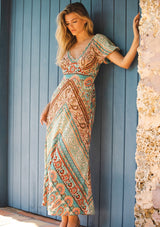 [Color: Jade/Natural] An image of a brunette model wearing a multi print bohemian maxi dress with brown heels for the fall season. A teal and green flowy dress with a v neckline, puff sleeves, and smocked back. A popular maxi dress for easy transition from summer to fall.