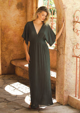 [Color: Military] An image of a blonde model wearing a classic casual military maxi dress. With half-length kimono sleeves, a plunging v neckline, a smocked elastic empire waist, side slits, and an open back with tie closure.