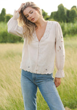 [Color: Buff] A blonde model wearing a beige blouse with a peter pan collar. A relaxed fit bohemian blouse with tonal embroidery, hook and eye front closure, long sleeves, and ruffle trim cuffs.