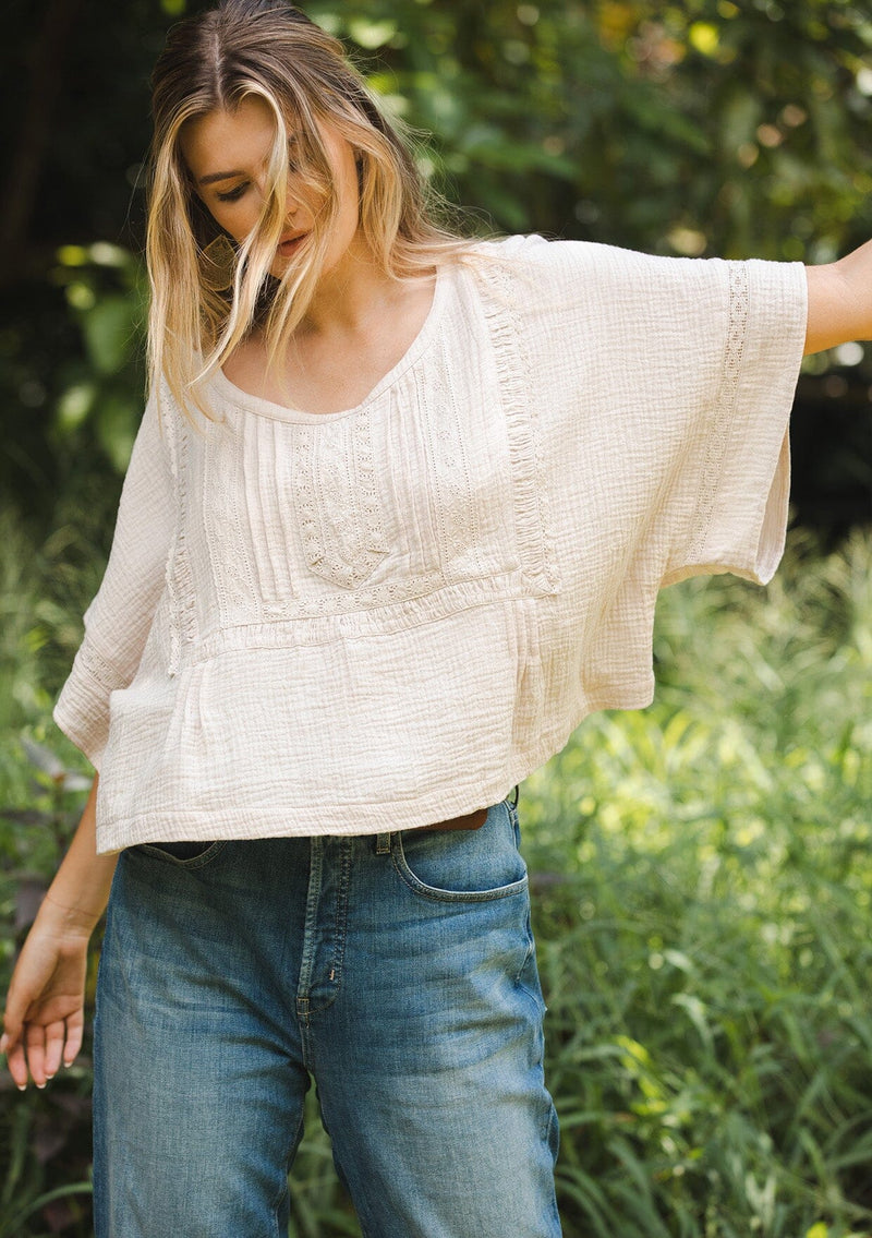 [Color: Natural] A blonde model wearing a soft cotton gauze top in beige natural. With a scoop neckline, embroidered front detail, and kimono sleeves. A relaxed fit top for lounging or a casual day out. Paired with denim jeans for a laid back style.