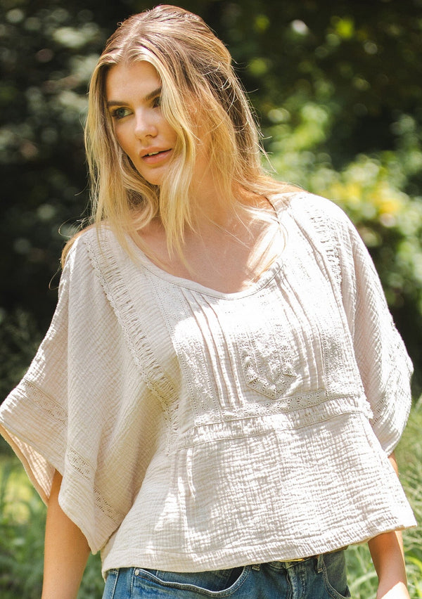 [Color: Natural] A blonde model wearing a soft cotton gauze top in beige natural. With a scoop neckline, embroidered front detail, and kimono sleeves. A relaxed fit top for lounging or a casual day out. Paired with denim jeans for a laid back style.