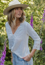 [Color: Vanilla] A blonde model wearing a textured cotton blouse in ivory white. With lace and crochet trims, functional button front, v neckline, and relaxed fit. A casual bohemian top paired with denim jeans.