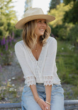 [Color: Vanilla] A blonde model wearing a textured cotton blouse in ivory white. With lace and crochet trims, functional button front, v neckline, and relaxed fit. A casual bohemian top paired with denim jeans.