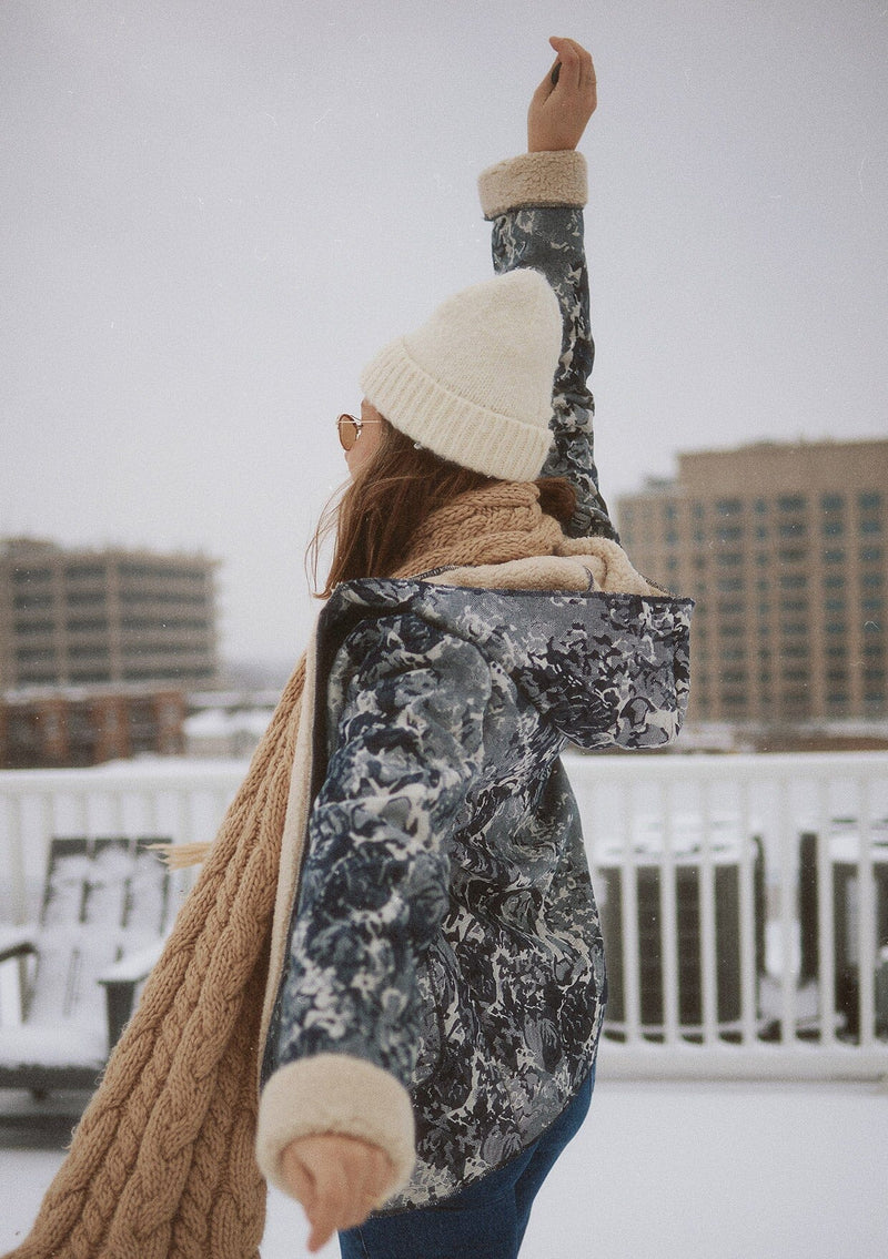 [Color: Denim Blue] A side-facing image of a blonde model wearing a denim floral jacket with a sherpa lining. The jacket features a cozy shawl collar, open front, patch pockets, long sleeves, and fold-over cuffs with exposed sherpa. A cold weather essential . 