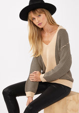 [Color: Natural/Black] A sitting image of a blonde model wearing a striped knit pullover with a bold contrast. Featuring a collared v-neckline, long sleeves, dropped shoulders, and a ribbed cuffs and hem. A relaxed knit sweater styled with black bottoms for the fall season. 