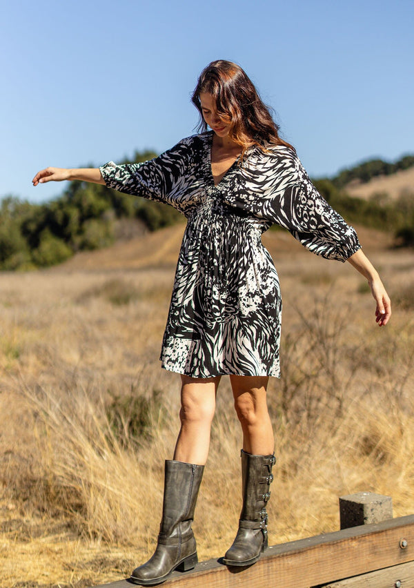 [Color: Black/Cream] A front facing image of a brunette model wearing a versatile black and ivory multi print mini dress. This long sleeve boho mini dress features a smocked neckline, smocked empire waist, and side pockets. Perfect for casual outings, vacation, or dinner dates.  