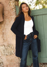 [Color: Navy] A navy blue cardigan with a fuzzy texture and soft touch. Features a hood, long sleeves, and patch pockets. A versatile cardigan layered with a white top for easy styling. Paired and styled with vintage denim and boots for the ultimate cozy look.