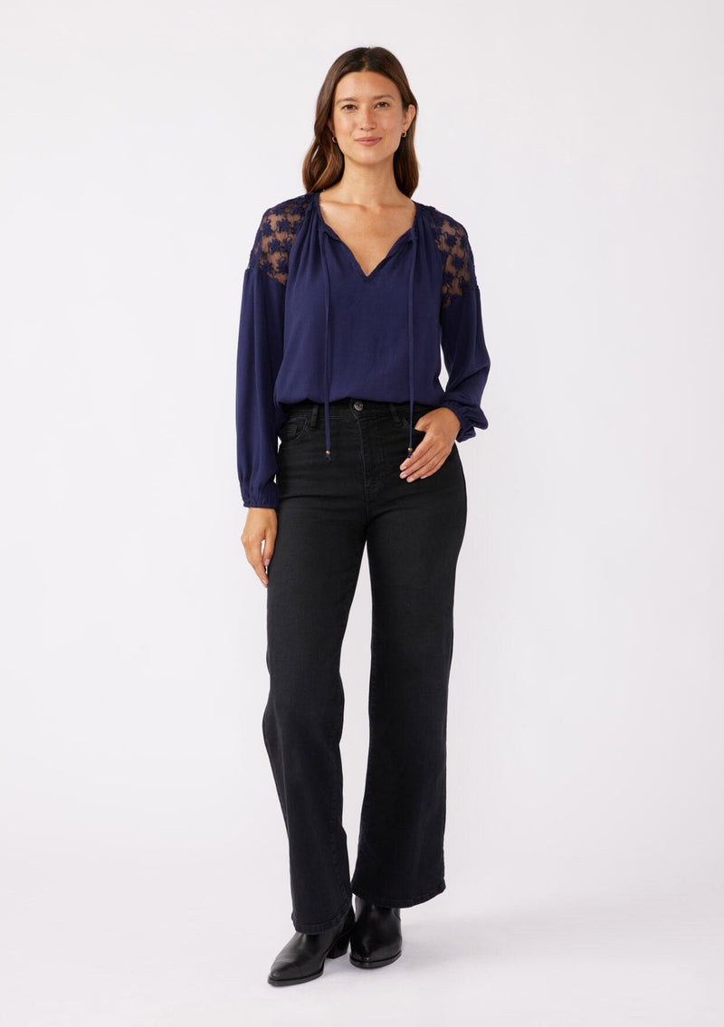 [Color: Navy] A front facing image of a brunette model wearing a navy blue bohemian fall blouse with long sleeves, a split v neckline with ties, and sheer embroidered mesh detail along the shoulders.