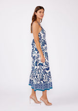 [Color: Vanilla/Navy] Brunette model wearing a blue and white floral tile print midi dress. A stunning dress with a flattering square neckline, sleeveless design, and an open tie back. A cute dress for vacation and warm weather occasions.