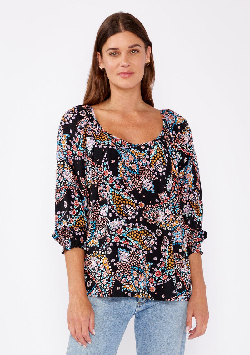 [Color: Black/Light Blue] A brunette woman wearing a multi color floral print top with long sleeves and a wide v neckline. A casual top tucked in styled with denim pants. A summer to fall style for casual outings. 