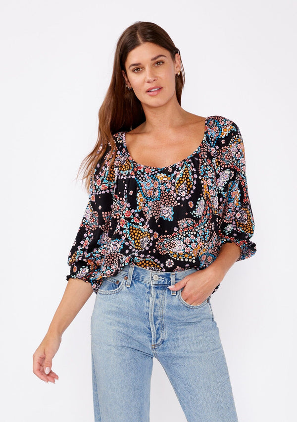 [Color: Black/Light Blue] A brunette woman wearing a multi color floral print top with long sleeves and a wide v neckline. A casual top tucked in styled with denim pants. A summer to fall style for casual outings. 