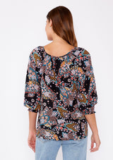 [Color: Black/Light Blue] A brunette woman wearing a multi color floral print top with long sleeves and a wide v neckline. A casual top tucked in styled with denim pants. A summer to fall style for casual outings. 