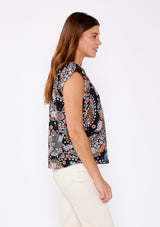 [Color: Black/Light Blue] An image of a brunette model wearing a multi color floral print bohemian top crafted from lightweight rayon fabric. With short cap sleeves, a split v neckline, and gathered details at the yoke. A summer to fall blouse perfect for casual outings. 